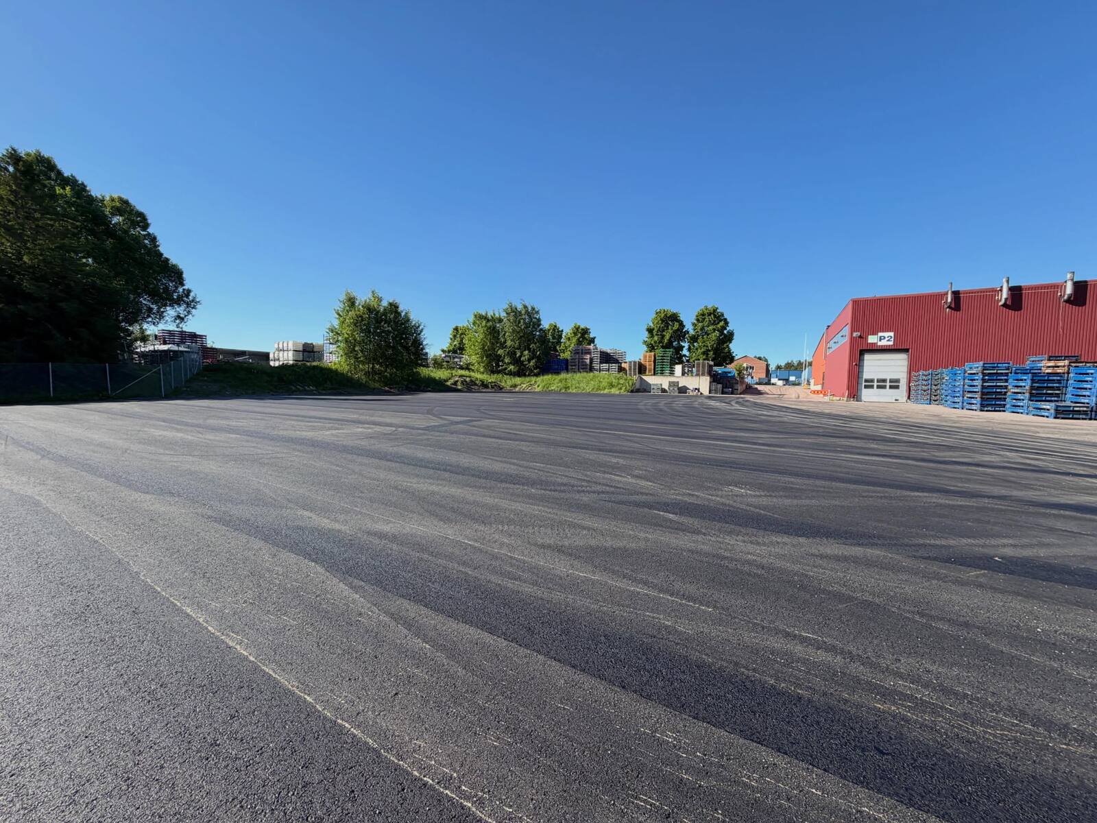 Nylagd asfalt på industriplan framför röd byggnad