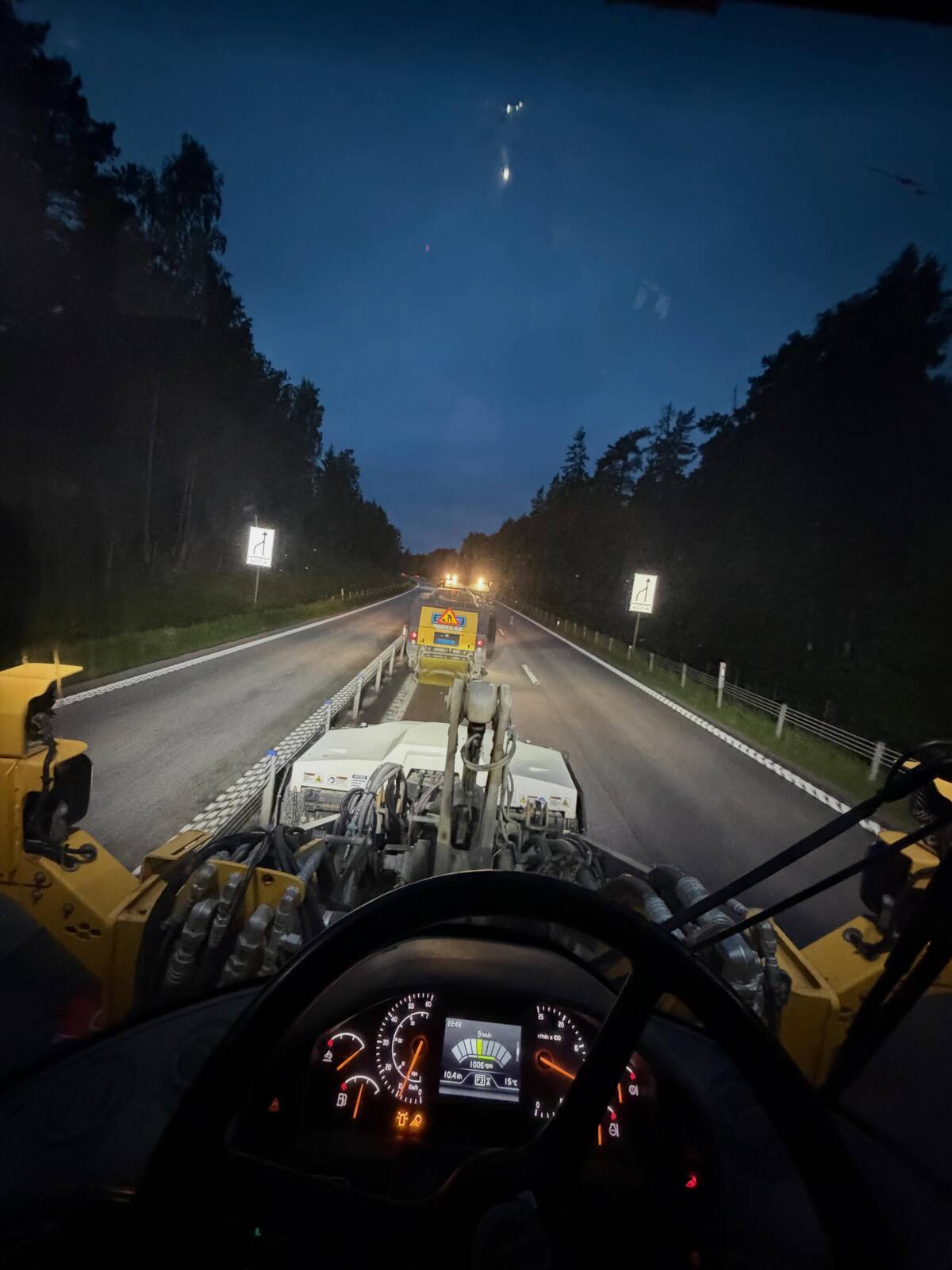 Sopmaskin från hytten som sopar E18 i mörkret med skog längs vägen